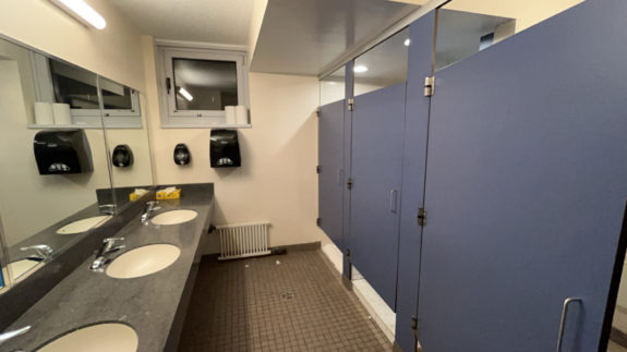 A photo of a Schapiro bathroom. On the right are three sinks and on the left are blue shower and bathroom stalls.